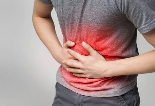 "Person holding their stomach in pain, with a blurred background of digestive system illustration"