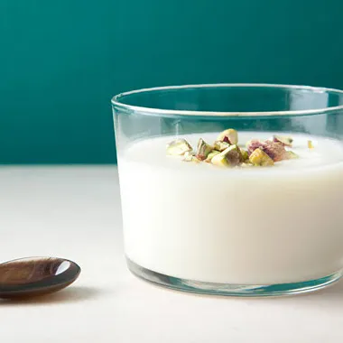 "Creamy milk pudding in a white cup with sprinkles and a spoon"