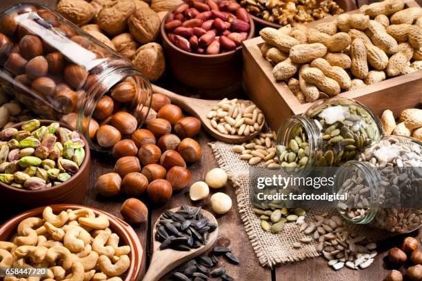 : "Assorted nuts and seeds, including almonds, pumpkin seeds, and chia seeds, on a wooden table"