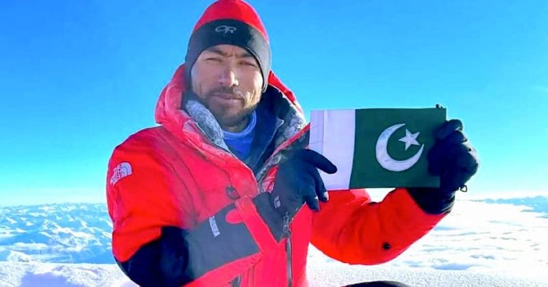 "Sirbaz Khan standing atop a mountain, Pakistani flag in hand"